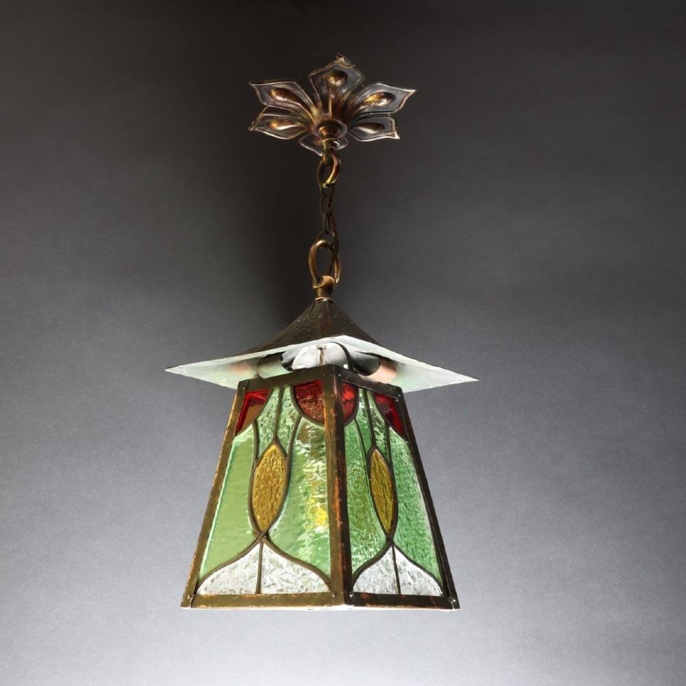An Arts and Crafts planished copper hanging lantern featuring leaded green, yellow, and clear glass panels suspended from a chain and floral ceiling rose. View III
