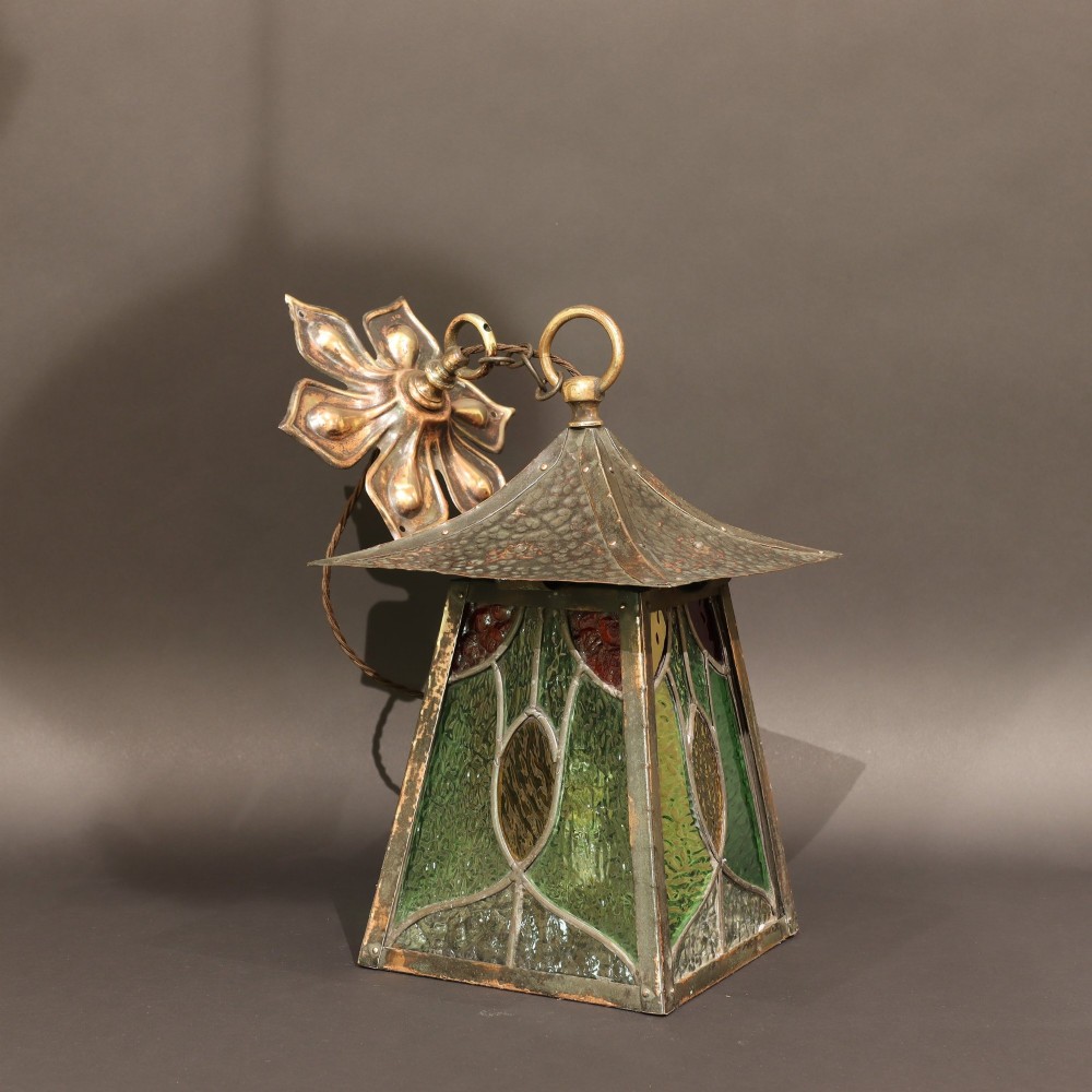 An Arts and Crafts planished copper hanging lantern featuring leaded green, yellow, and clear glass panels suspended from a chain and floral ceiling rose. View IV