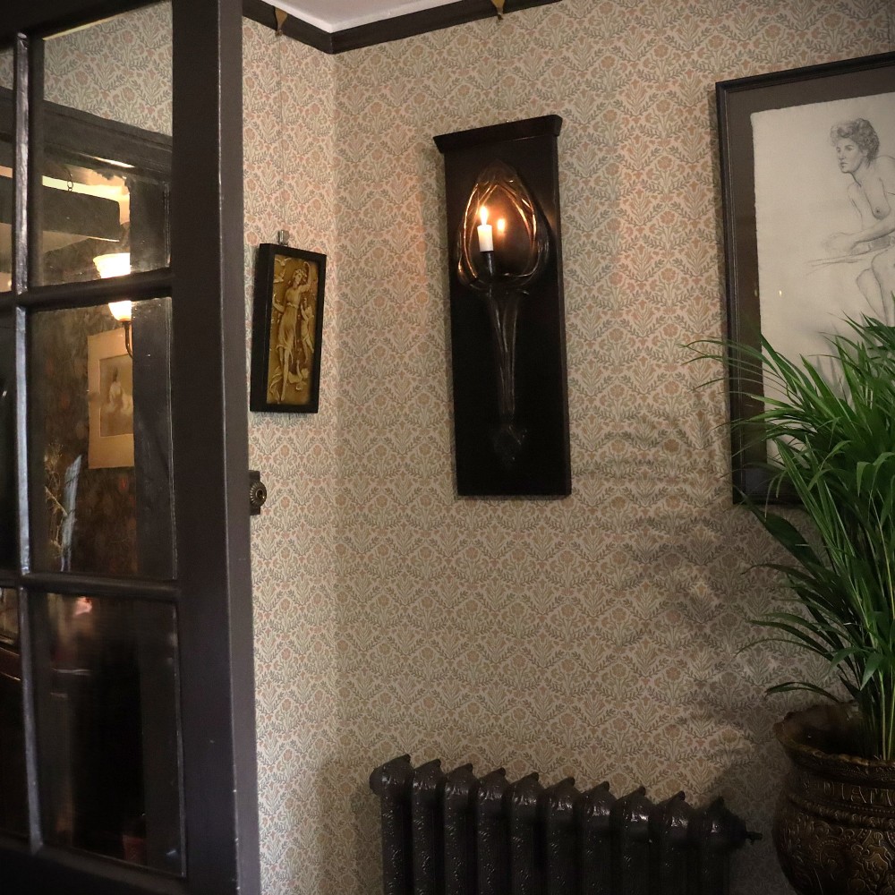 A patinated copper wall sconce with stylized Art Nouveau repousse details mounted on a dark rectangular wooden backboard. View II