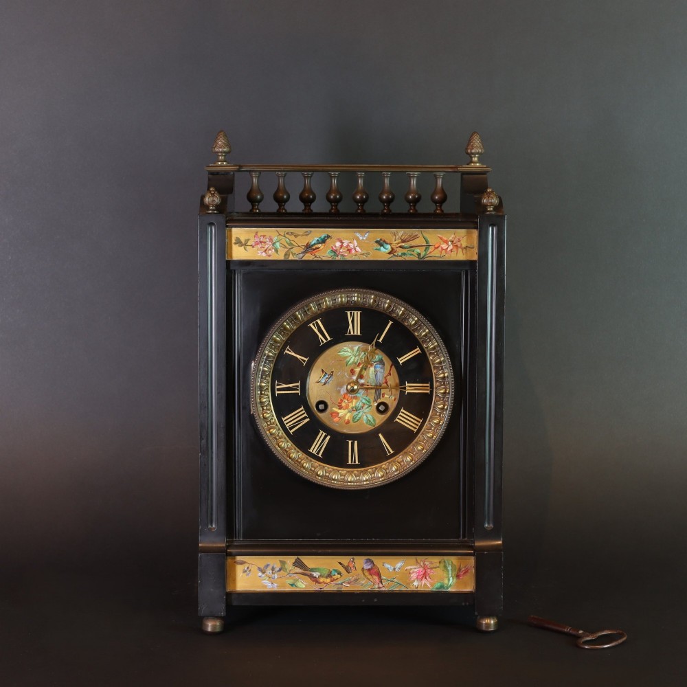 An Aesthetic movement black slate mantel clock featuring hand-painted botanical panels, brass spindle gallery, and a circular dial with Roman numerals.
