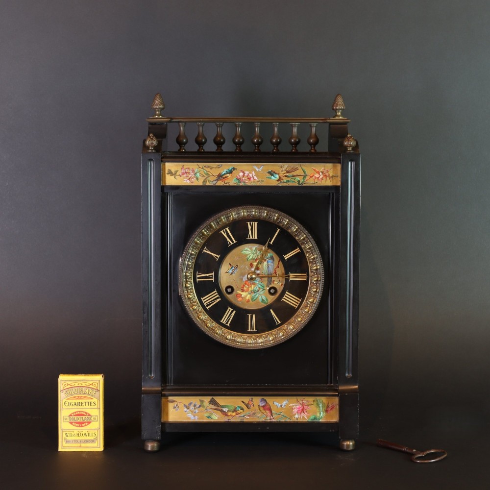 An Aesthetic movement black slate mantel clock featuring hand-painted botanical panels, brass spindle gallery, and a circular dial with Roman numerals. View IV