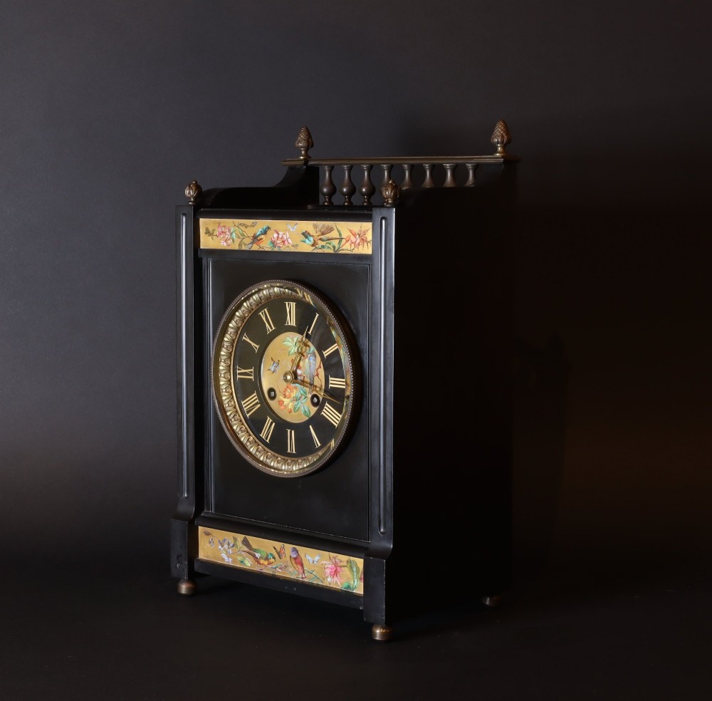 An Aesthetic movement black slate mantel clock featuring hand-painted botanical panels, brass spindle gallery, and a circular dial with Roman numerals. View V
