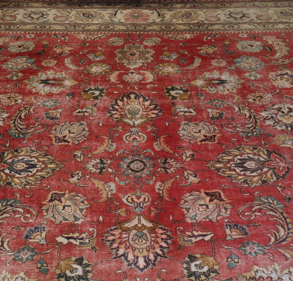 An antique hand-knotted red wool carpet featuring detailed floral palmettes and a light cream border.