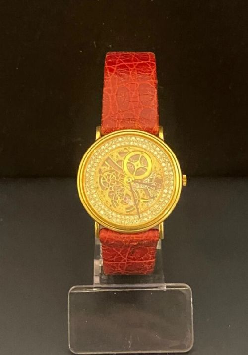 fig 1. A vintage round wristwatch with an 18k gold case surrounded by diamonds, featuring an openwork skeleton movement and a red leather strap.