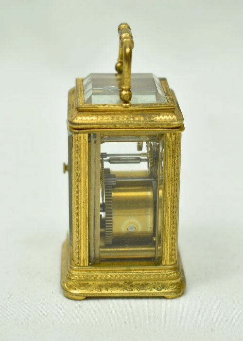 fig 1. A miniature French gilt brass carriage clock with ornate scroll engraving and a white enamel dial, shown inside its open leather travelling case.