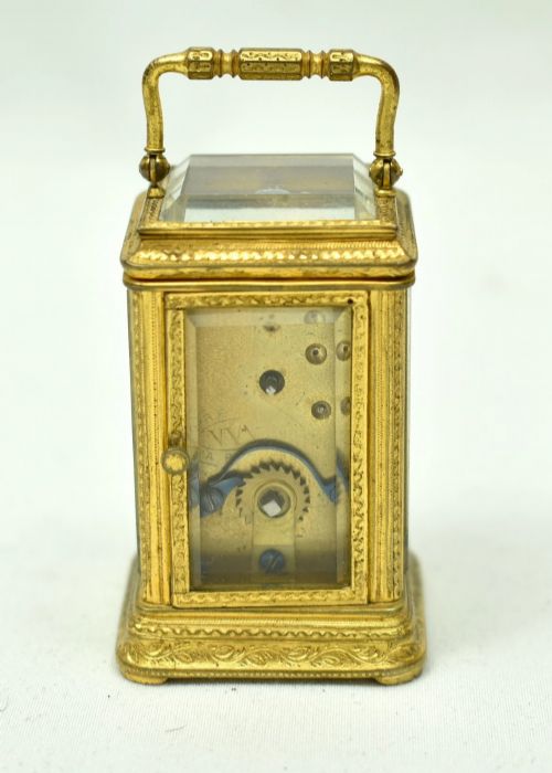 fig 2. A miniature French gilt brass carriage clock with ornate scroll engraving and a white enamel dial, shown inside its open leather travelling case.