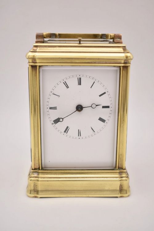 fig 1. A rectangular polished brass French carriage clock featuring a doucine style case, top carrying handle, white enamel dial with Roman numerals, and glass side panels.