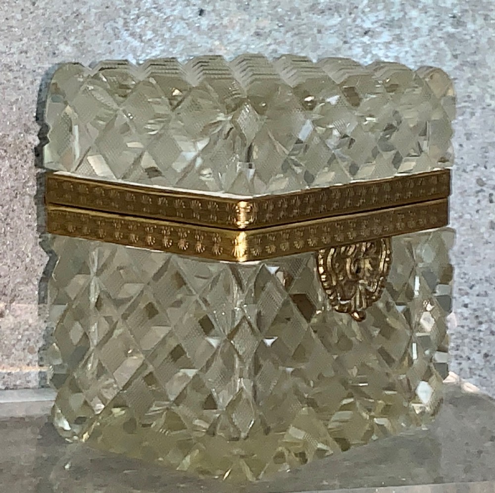 A square diamond-cut clear glass casket box featuring a hinged gilt-bronze rim with an ornate metal clasp.
