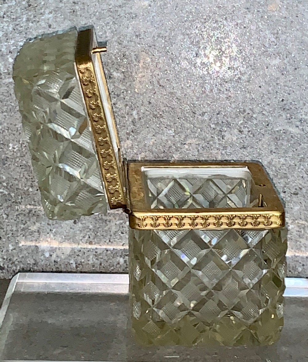 A square diamond-cut clear glass casket box featuring a hinged gilt-bronze rim with an ornate metal clasp. View X