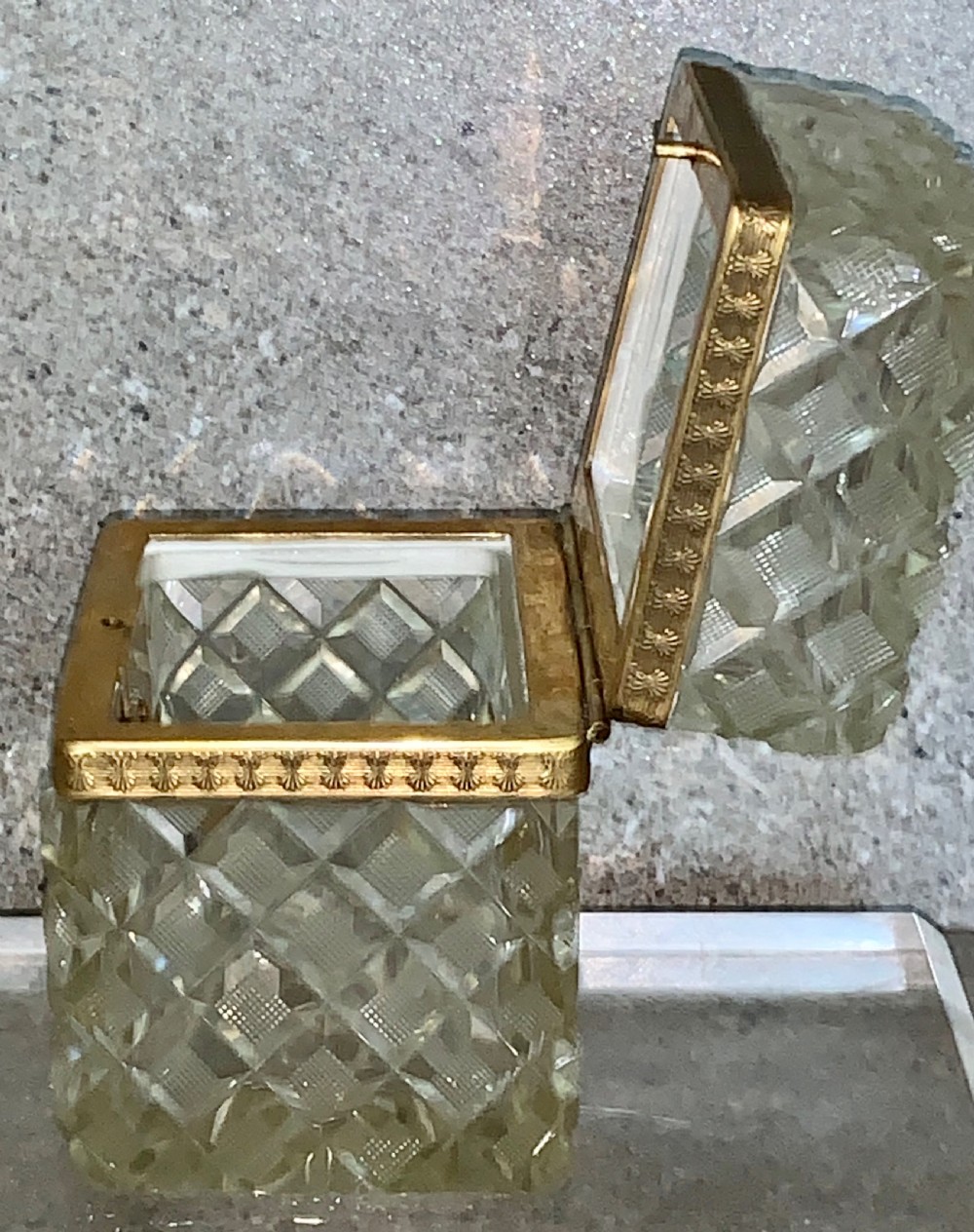 A square diamond-cut clear glass casket box featuring a hinged gilt-bronze rim with an ornate metal clasp. View XII