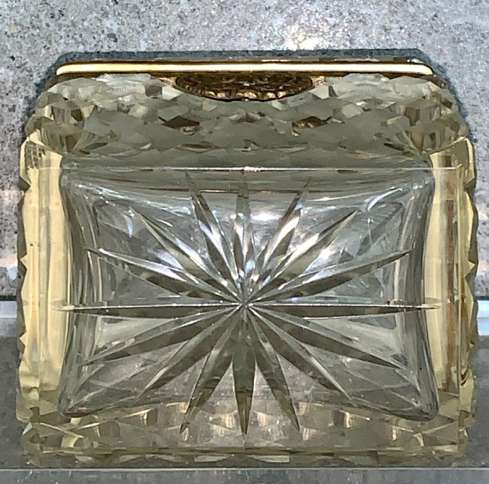 A square diamond-cut clear glass casket box featuring a hinged gilt-bronze rim with an ornate metal clasp. View XIV