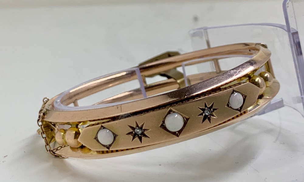 A Victorian 9ct rose gold hinged bangle with star-set diamonds and cabochon opals arranged on a central tapered panel. View III