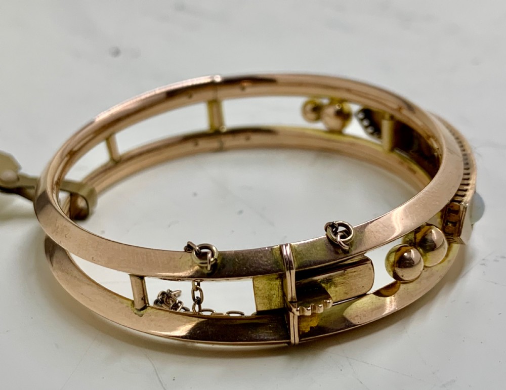 A Victorian 9ct rose gold hinged bangle with star-set diamonds and cabochon opals arranged on a central tapered panel. View IV