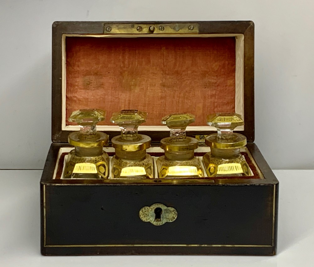An open dark wood casket with brass stringing and silk lining containing four gilded crystal scent bottles with faceted stoppers.