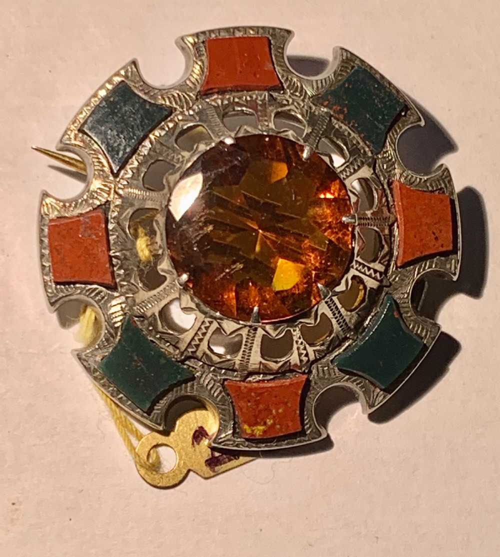 A circular Victorian silver Scottish brooch inlaid with red and green agate panels surrounding a large central faceted amber citrine stone. View II