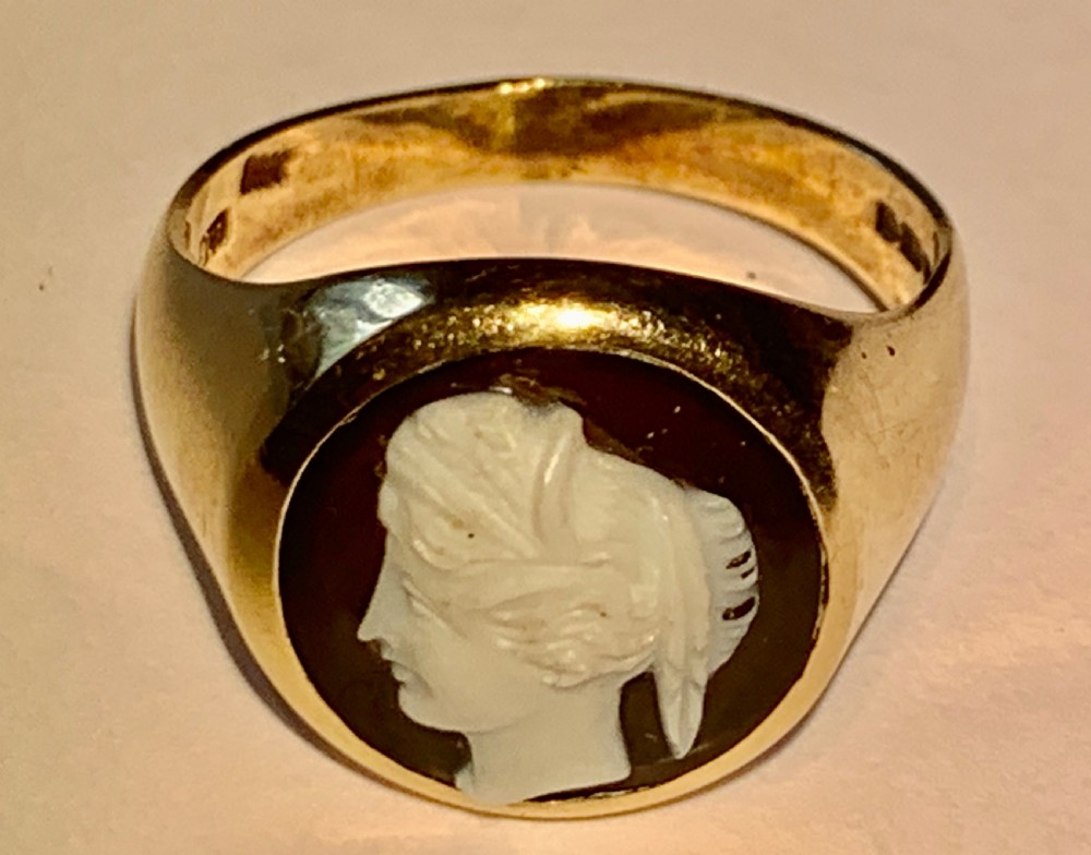 A Victorian 9ct yellow gold signet style ring set with an oval carved agate cameo depicting a white classical female profile against a dark background.