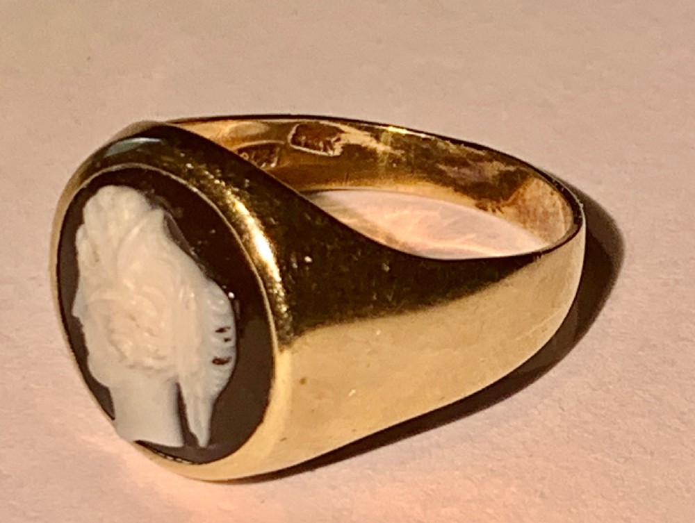 A Victorian 9ct yellow gold signet style ring set with an oval carved agate cameo depicting a white classical female profile against a dark background. View V