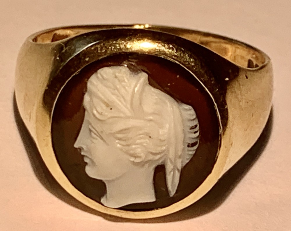 A Victorian 9ct yellow gold signet style ring set with an oval carved agate cameo depicting a white classical female profile against a dark background. View VIII