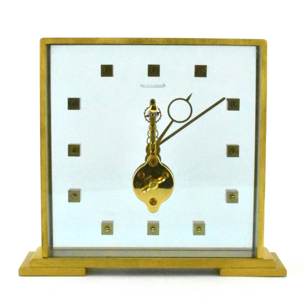A mid-century Jaeger-LeCoultre brass and glass square mantel clock featuring a visible internal skeleton movement and square brass hour markers.