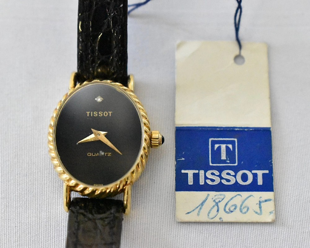 A vintage Tissot ladies wristwatch featuring an oval 18ct gold rope-twist bezel, a black dial with a single diamond marker at twelve oclock, and a black leather strap.