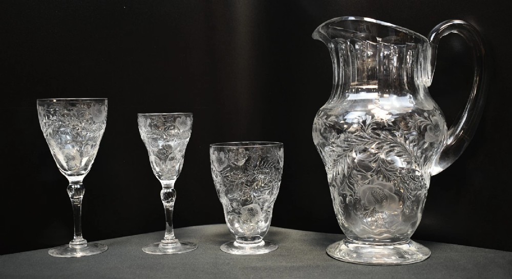 A clear lead crystal drinking set comprising a large floral-engraved pitcher alongside three matching wine and tumbler glasses.