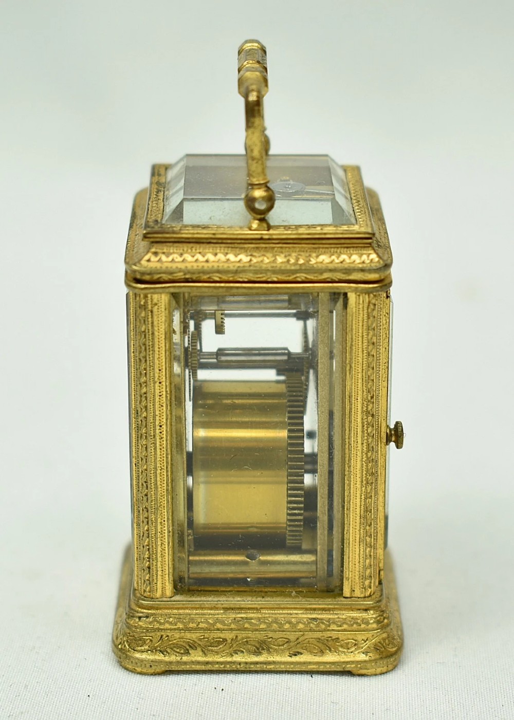 A miniature French gilt brass carriage clock with ornate scroll engraving and a white enamel dial, shown inside its open leather travelling case. View V