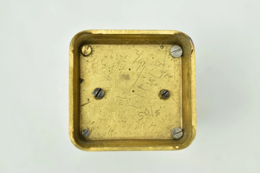 A miniature French gilt brass carriage clock with ornate scroll engraving and a white enamel dial, shown inside its open leather travelling case. View VII