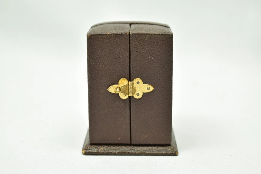 A miniature French gilt brass carriage clock with ornate scroll engraving and a white enamel dial, shown inside its open leather travelling case. View IX