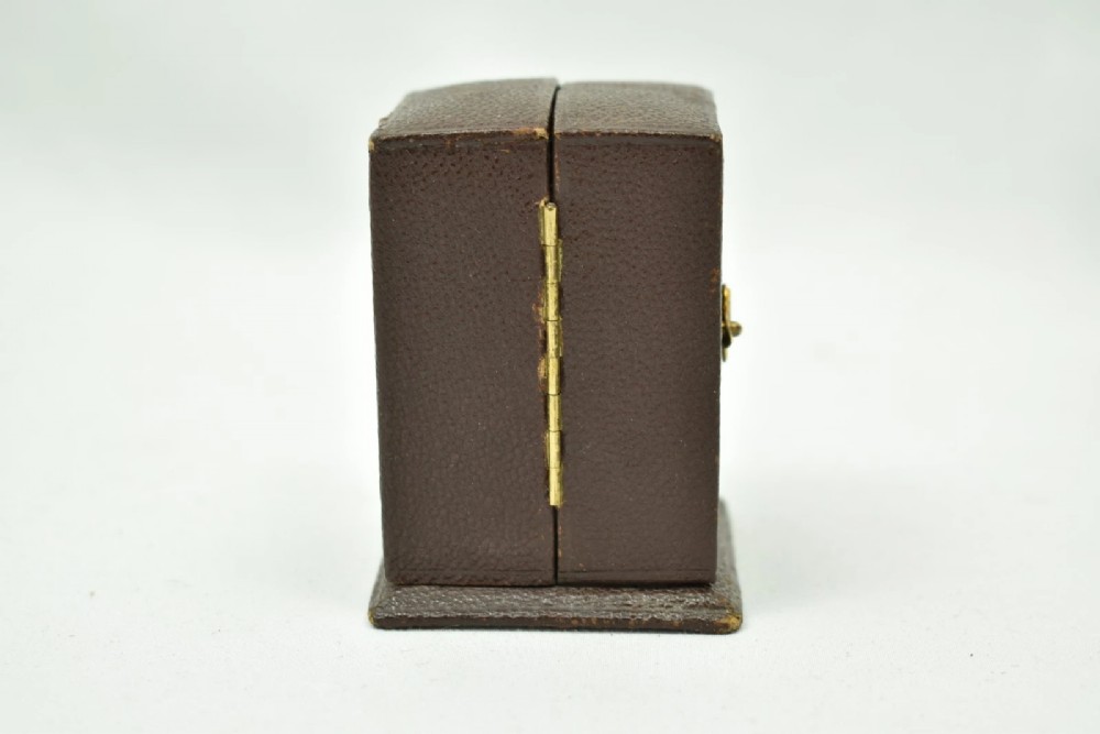 A miniature French gilt brass carriage clock with ornate scroll engraving and a white enamel dial, shown inside its open leather travelling case. View XI