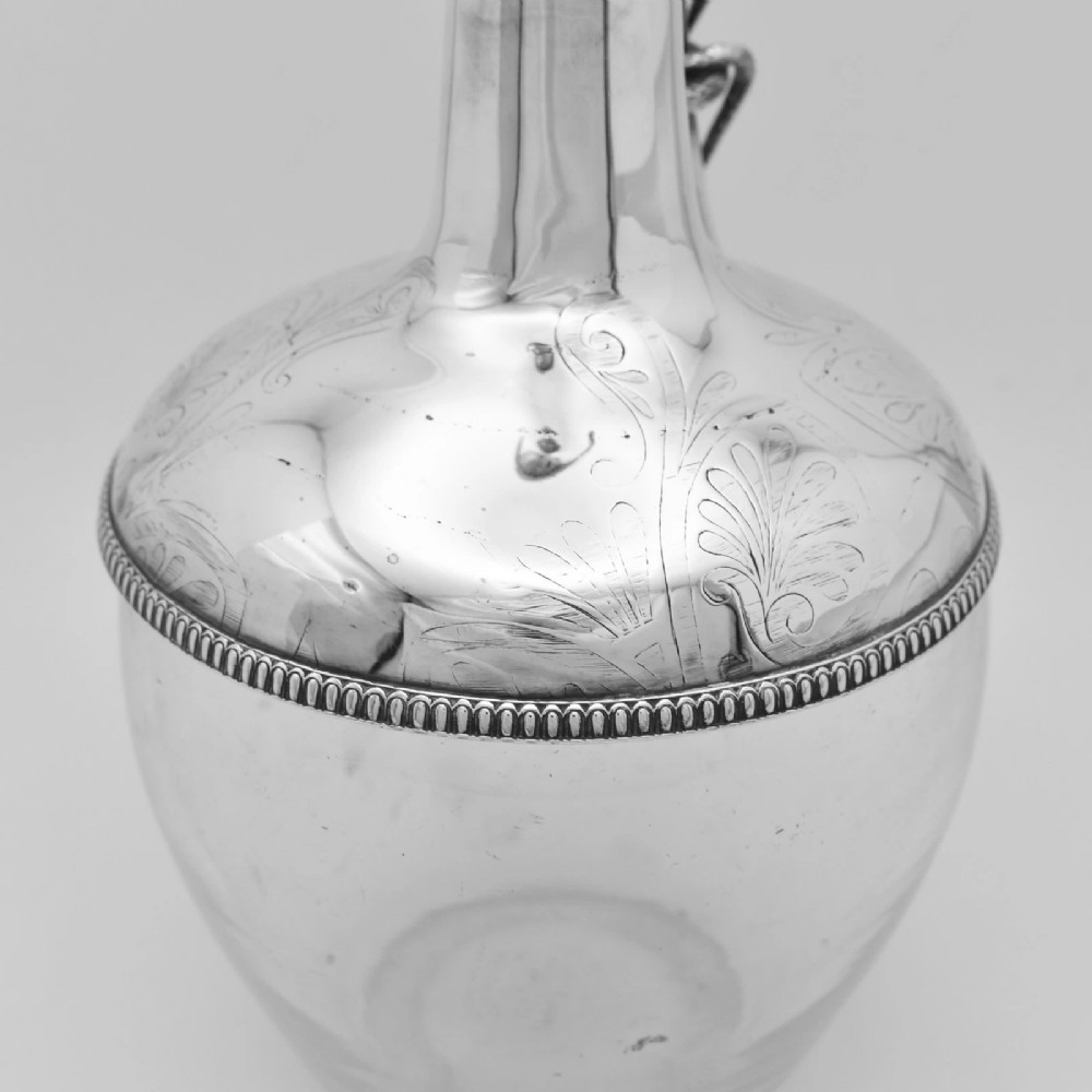 A pair of nineteenth-century clear crystal claret jugs featuring engraved silver mounts, tall necks, round stoppers, and silver handles shaped as entwined serpents. View II