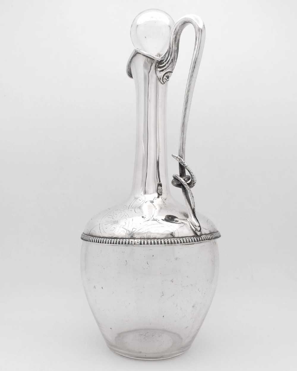 A pair of nineteenth-century clear crystal claret jugs featuring engraved silver mounts, tall necks, round stoppers, and silver handles shaped as entwined serpents. View X