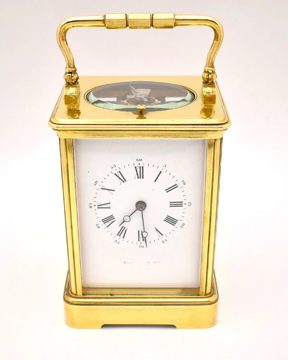 An antique French brass carriage clock featuring a hinged carrying handle, clear glass viewing windows, and a white enamel dial with Roman numerals.