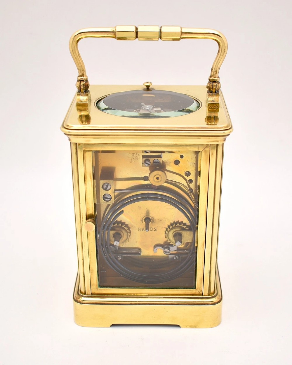 An antique French brass carriage clock featuring a hinged carrying handle, clear glass viewing windows, and a white enamel dial with Roman numerals. View III