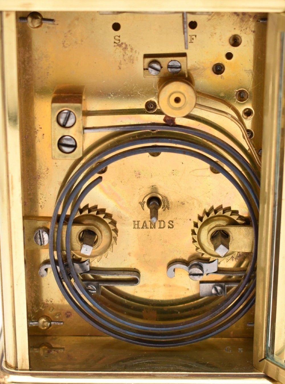 An antique French brass carriage clock featuring a hinged carrying handle, clear glass viewing windows, and a white enamel dial with Roman numerals. View IV