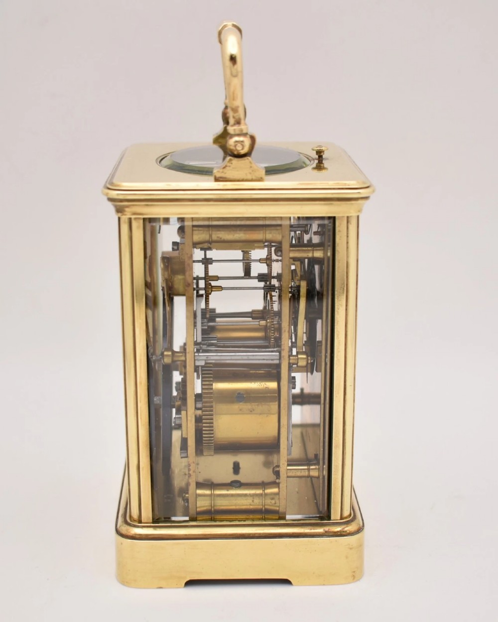 An antique French brass carriage clock featuring a hinged carrying handle, clear glass viewing windows, and a white enamel dial with Roman numerals. View V