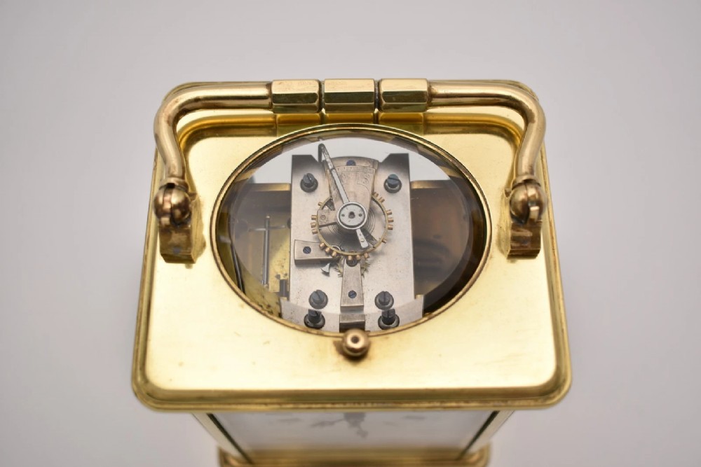 An antique French brass carriage clock featuring a hinged carrying handle, clear glass viewing windows, and a white enamel dial with Roman numerals. View VI