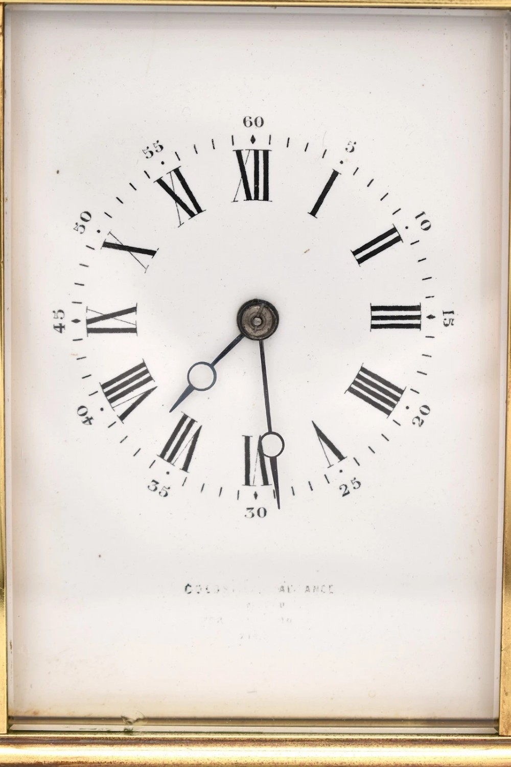 An antique French brass carriage clock featuring a hinged carrying handle, clear glass viewing windows, and a white enamel dial with Roman numerals. View VII