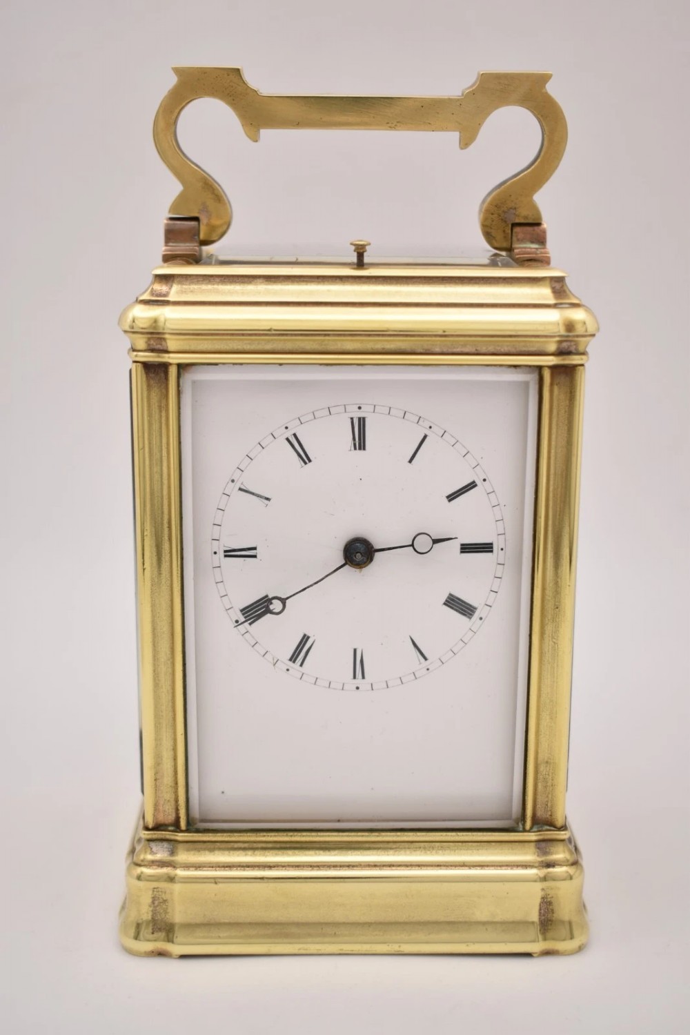 A rectangular polished brass French carriage clock featuring a doucine style case, top carrying handle, white enamel dial with Roman numerals, and glass side panels.