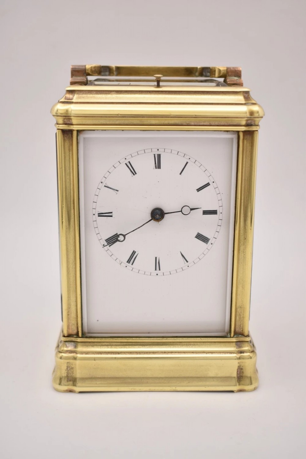 A rectangular polished brass French carriage clock featuring a doucine style case, top carrying handle, white enamel dial with Roman numerals, and glass side panels. View II