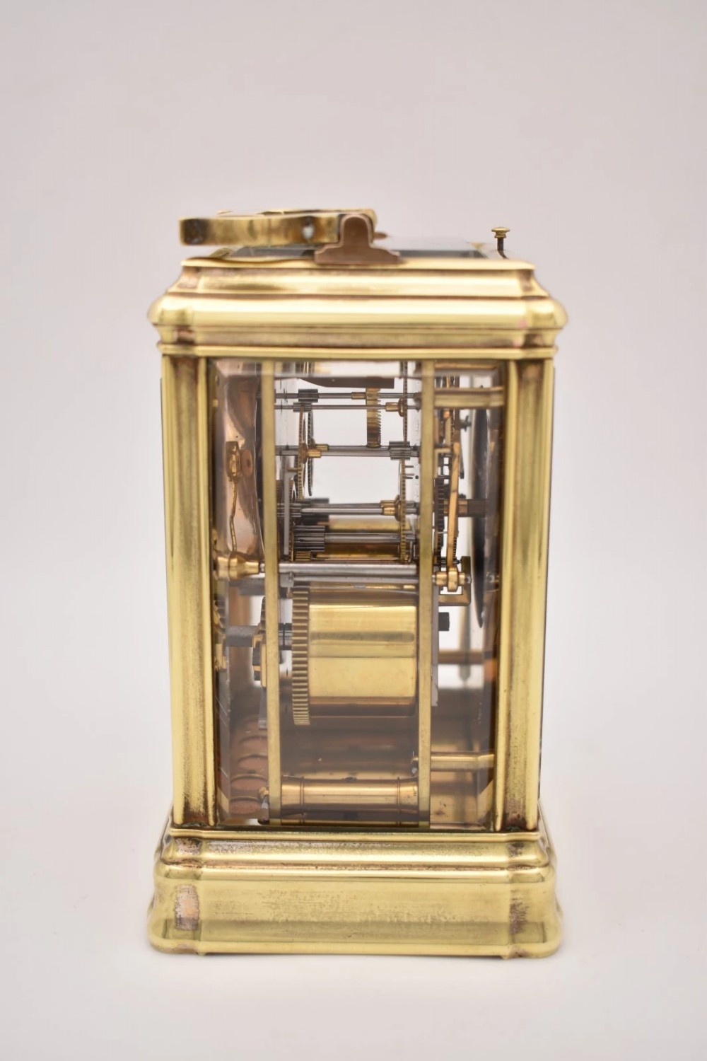 A rectangular polished brass French carriage clock featuring a doucine style case, top carrying handle, white enamel dial with Roman numerals, and glass side panels. View III