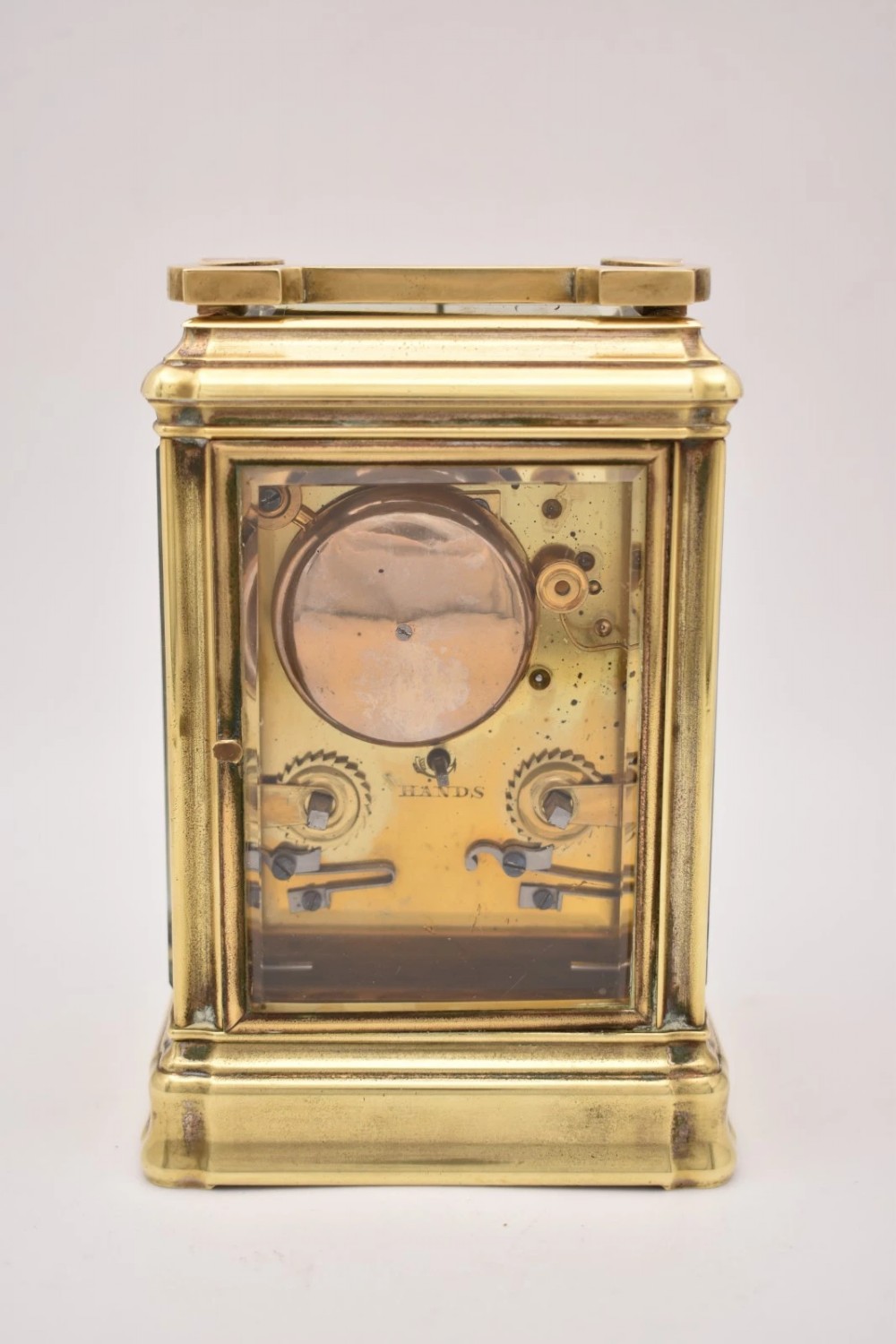 A rectangular polished brass French carriage clock featuring a doucine style case, top carrying handle, white enamel dial with Roman numerals, and glass side panels. View IV