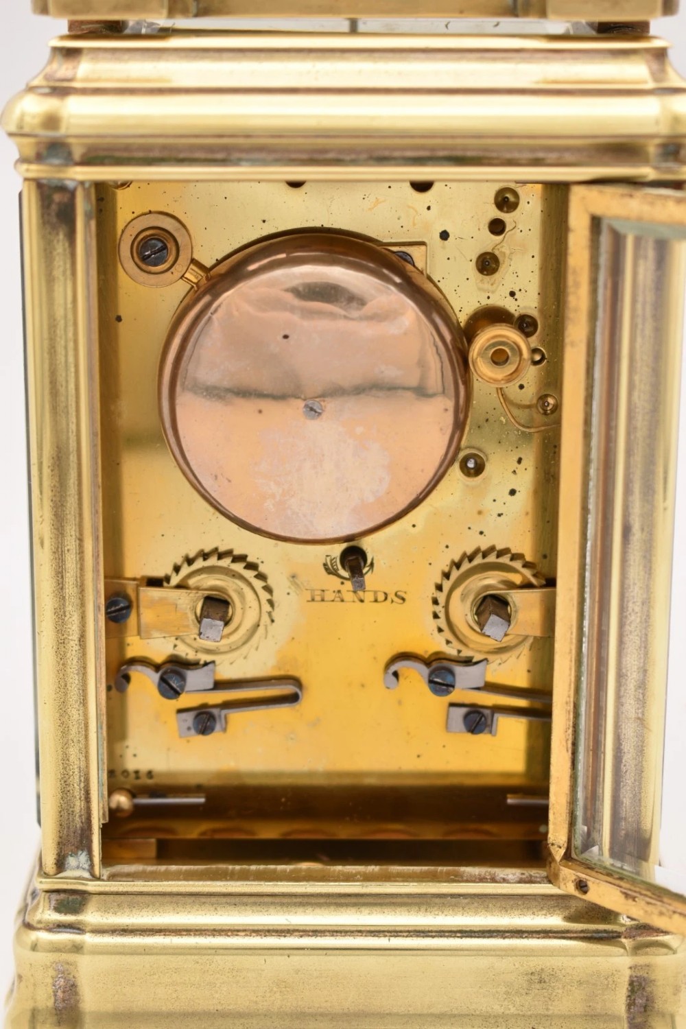 A rectangular polished brass French carriage clock featuring a doucine style case, top carrying handle, white enamel dial with Roman numerals, and glass side panels. View V
