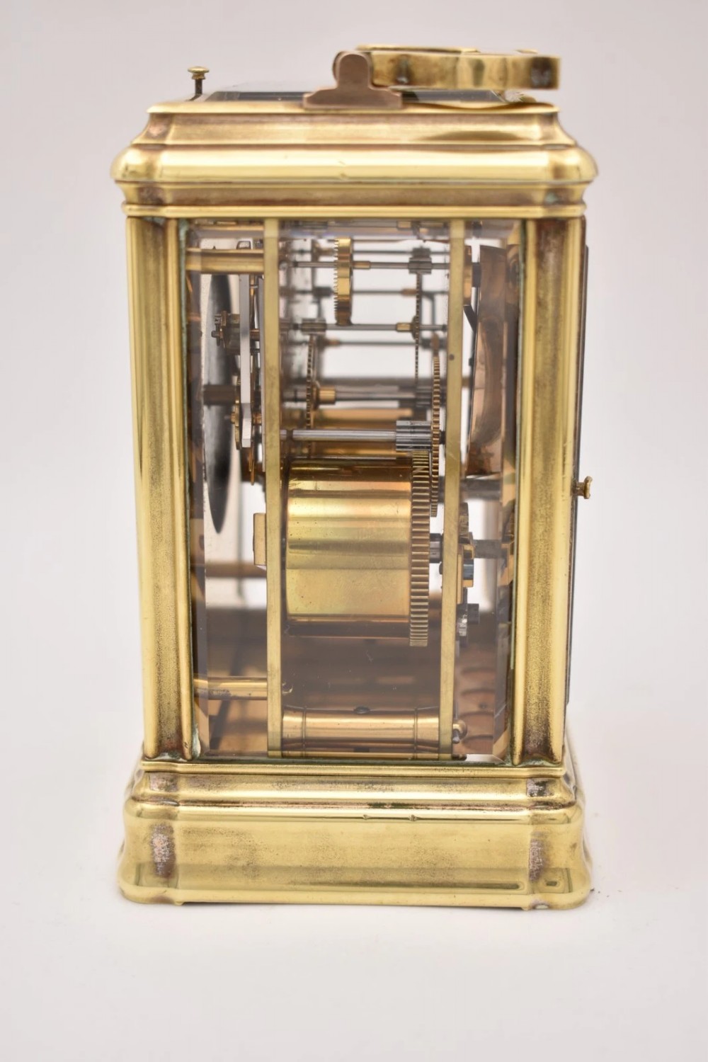 A rectangular polished brass French carriage clock featuring a doucine style case, top carrying handle, white enamel dial with Roman numerals, and glass side panels. View VI