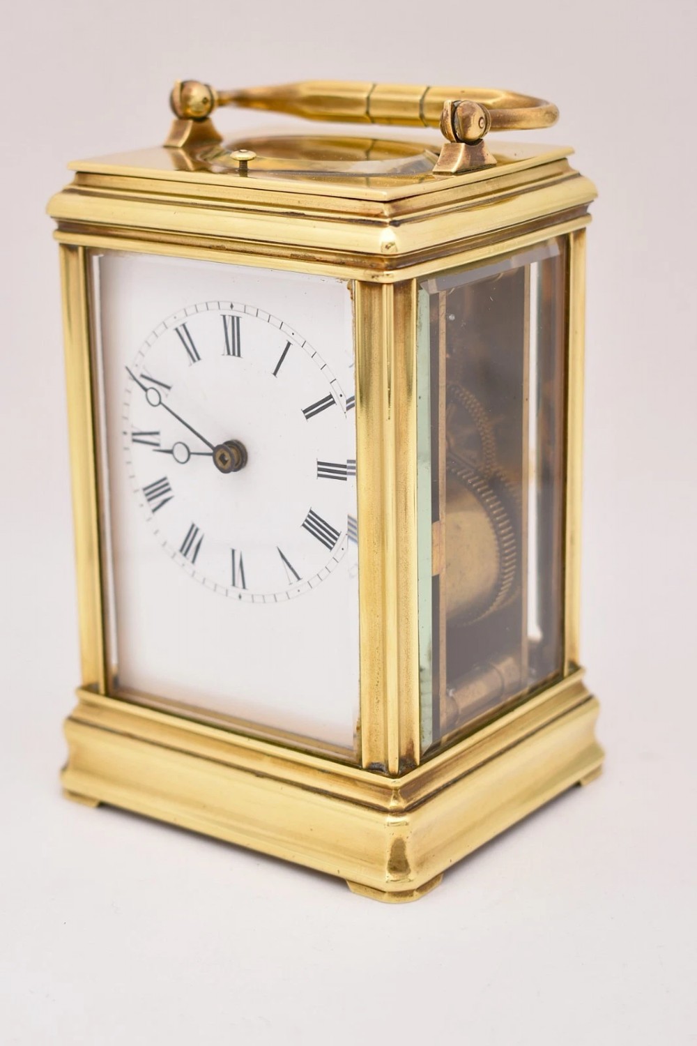 A late nineteenth-century French brass gorge case carriage clock featuring a white enamel dial with Roman numerals and a hinged top carrying handle. View VI