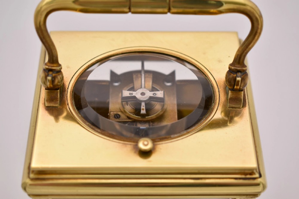 A late nineteenth-century French brass gorge case carriage clock featuring a white enamel dial with Roman numerals and a hinged top carrying handle. View IX