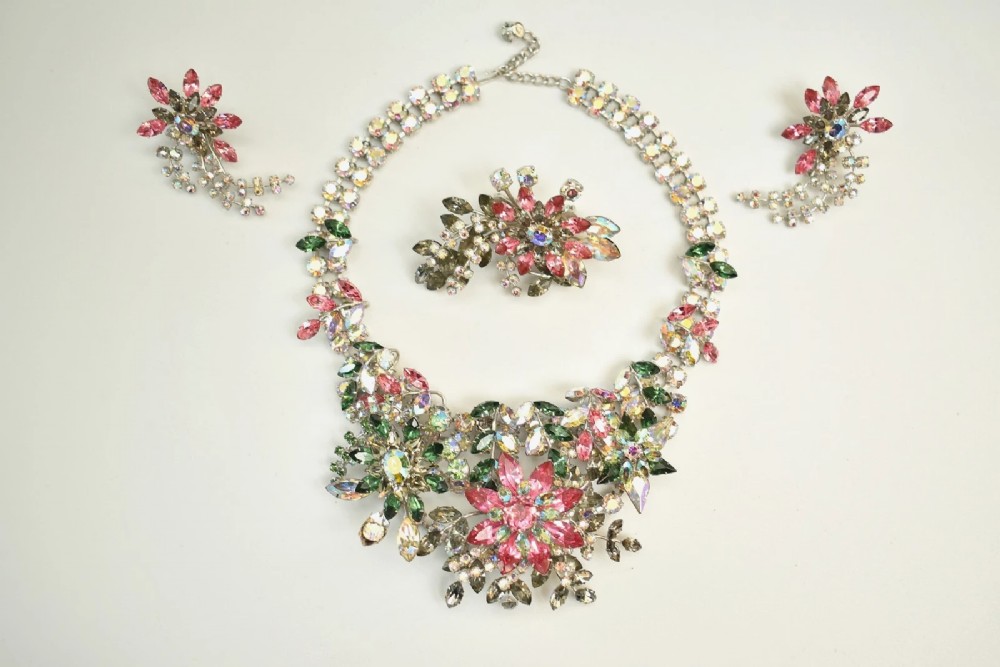 A 1950s Christian Dior costume jewellery parure set featuring a necklace, brooch, and clip-on earrings with pink, green, and aurora borealis crystal floral clusters.