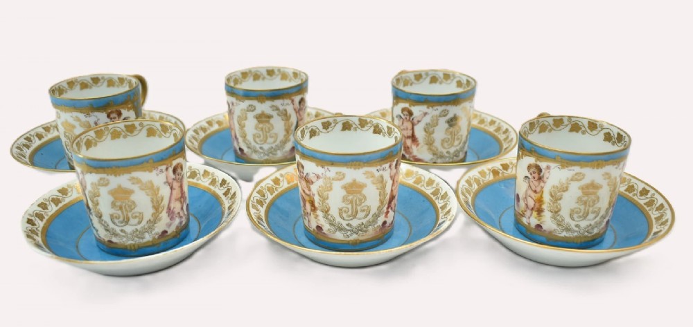 A six-piece set of white and sky-blue French porcelain demitasse cups and saucers decorated with gilded royal monograms, cherubs, and leaf borders.