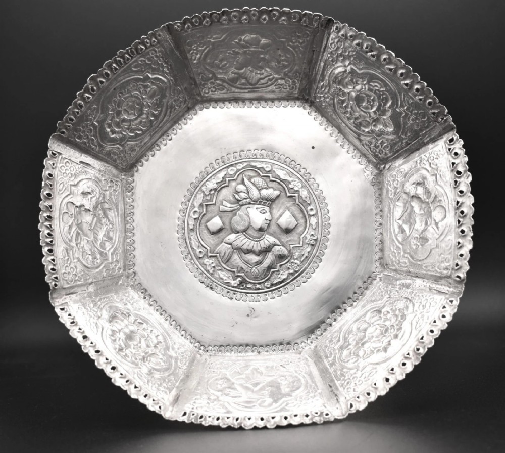 An octagonal antique silver repousse tazza featuring a central raised portrait medallion, intricate chased foliate side panels, and a pierced scalloped border.
