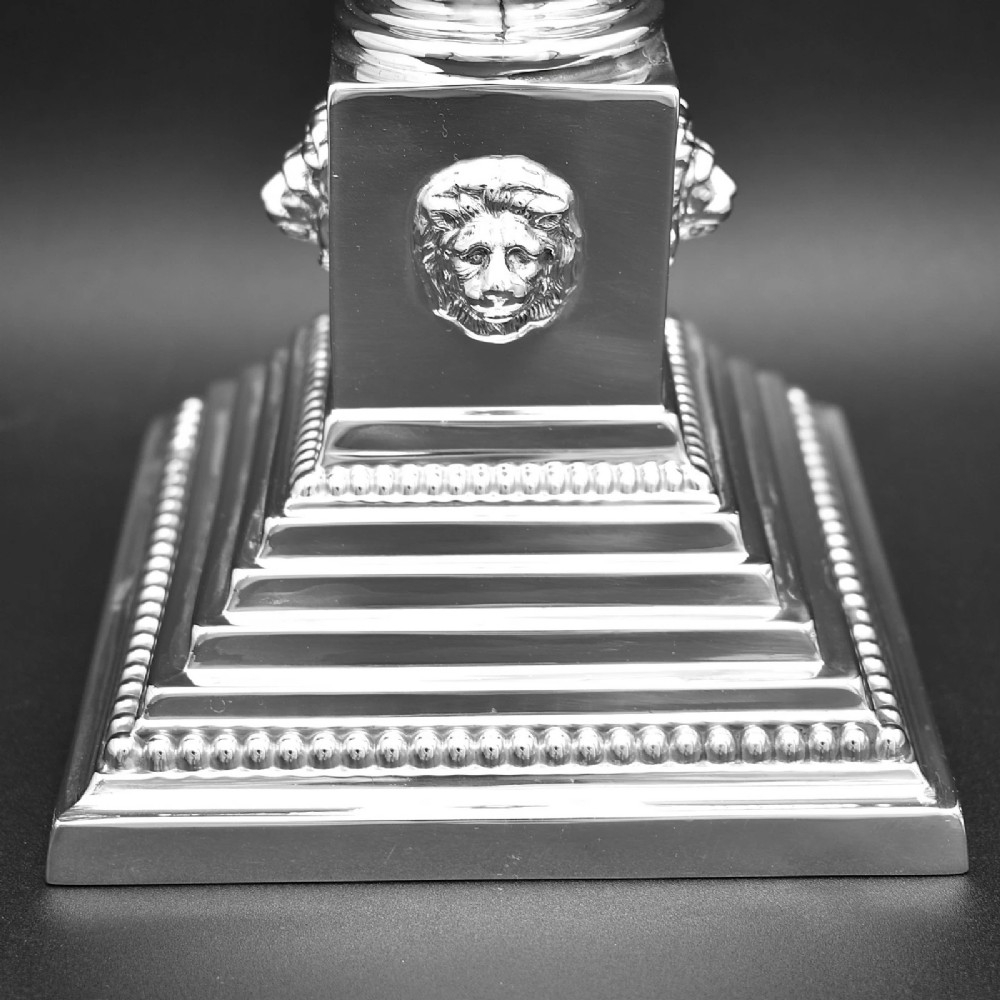 A pair of sterling silver candlesticks featuring fluted Corinthian columns, acanthus leaf capitals, lion mask motifs, and stepped square bases with beaded edging. View IV