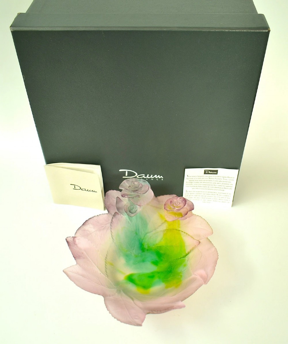 A Daum France pate de verre crystal rose bowl shaped like a pink blossom with green leaves, displayed alongside its original presentation box.